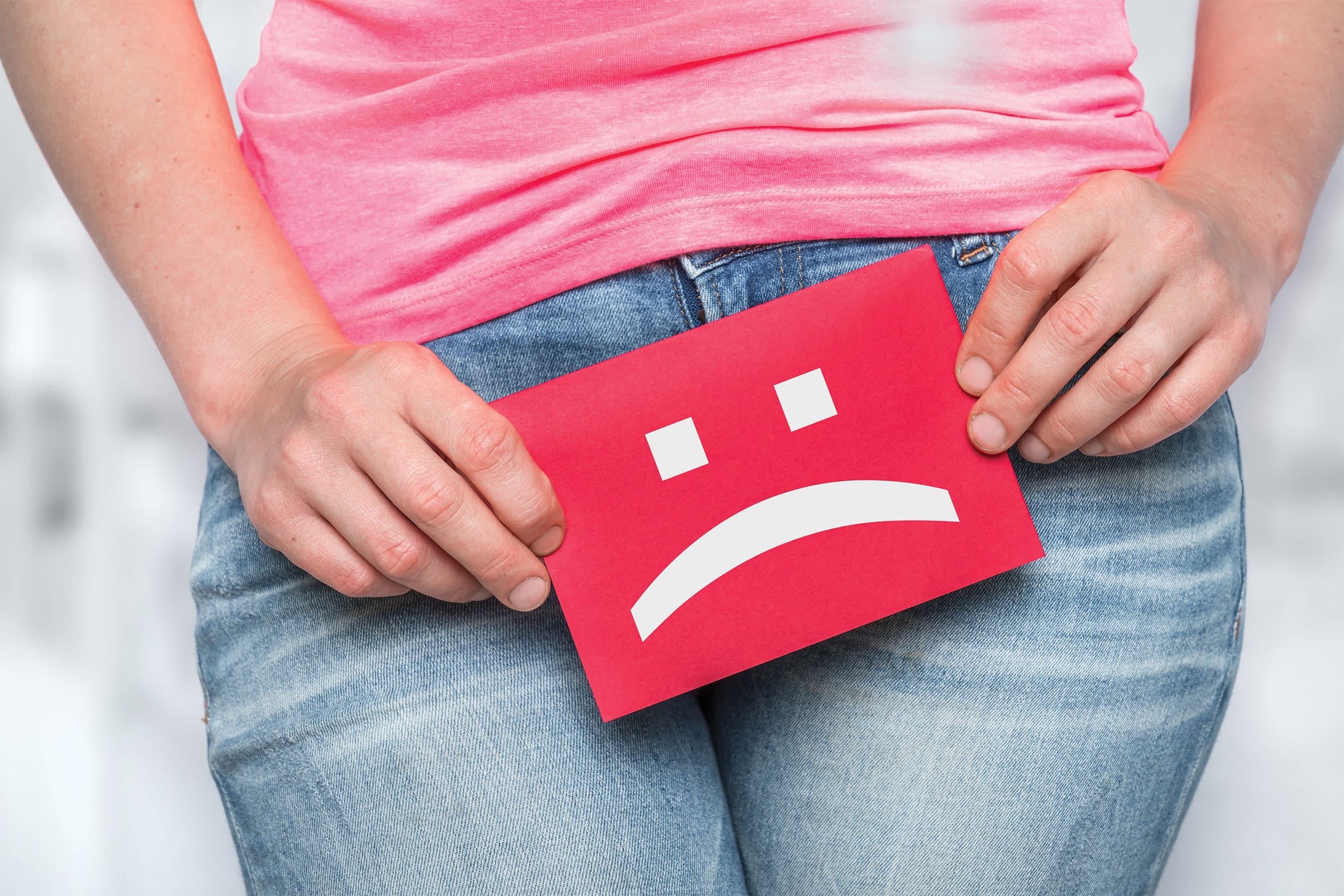 Woman holding a red sad face icon over her lower abdomen, indicating menstrual or pelvic discomfort.